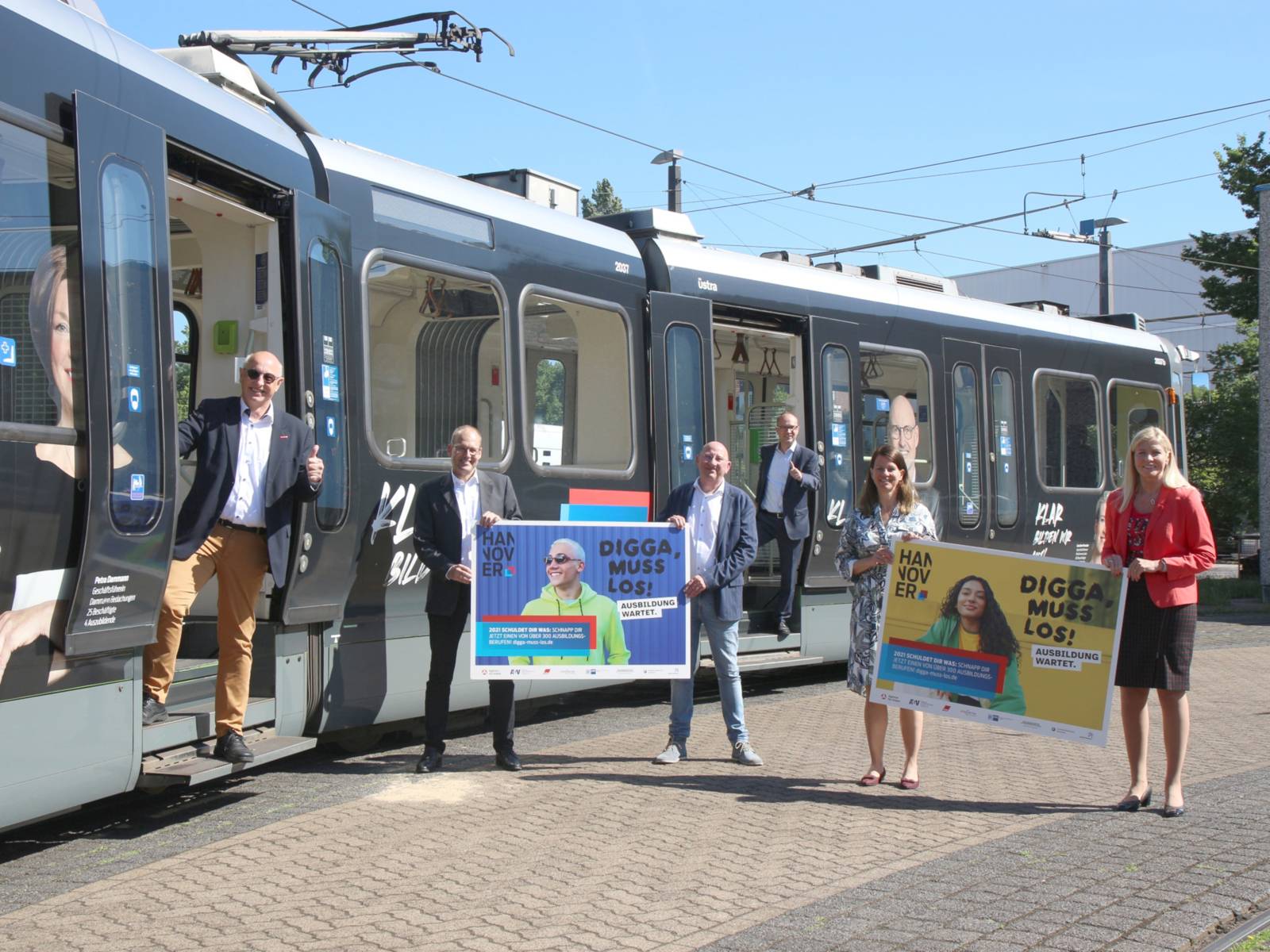 Zwei Frauen und vier Männer haben sich an einem Stadtbahnzug postiert. Es werden zwei Plakate gehalten und die Türen der Bahn sind geöffnet.
